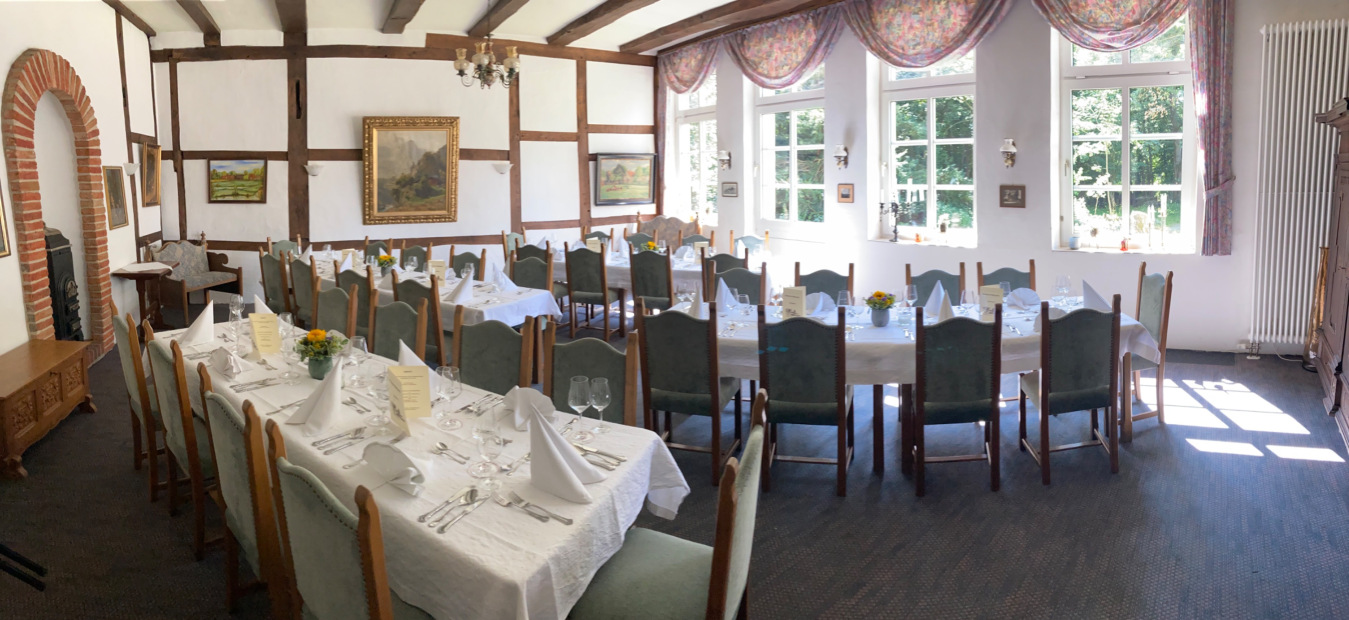 Fachwerkstube mit gedeckter langer Tafel, grünen Stühlen, Backsteinbogen und großer Fensterfront